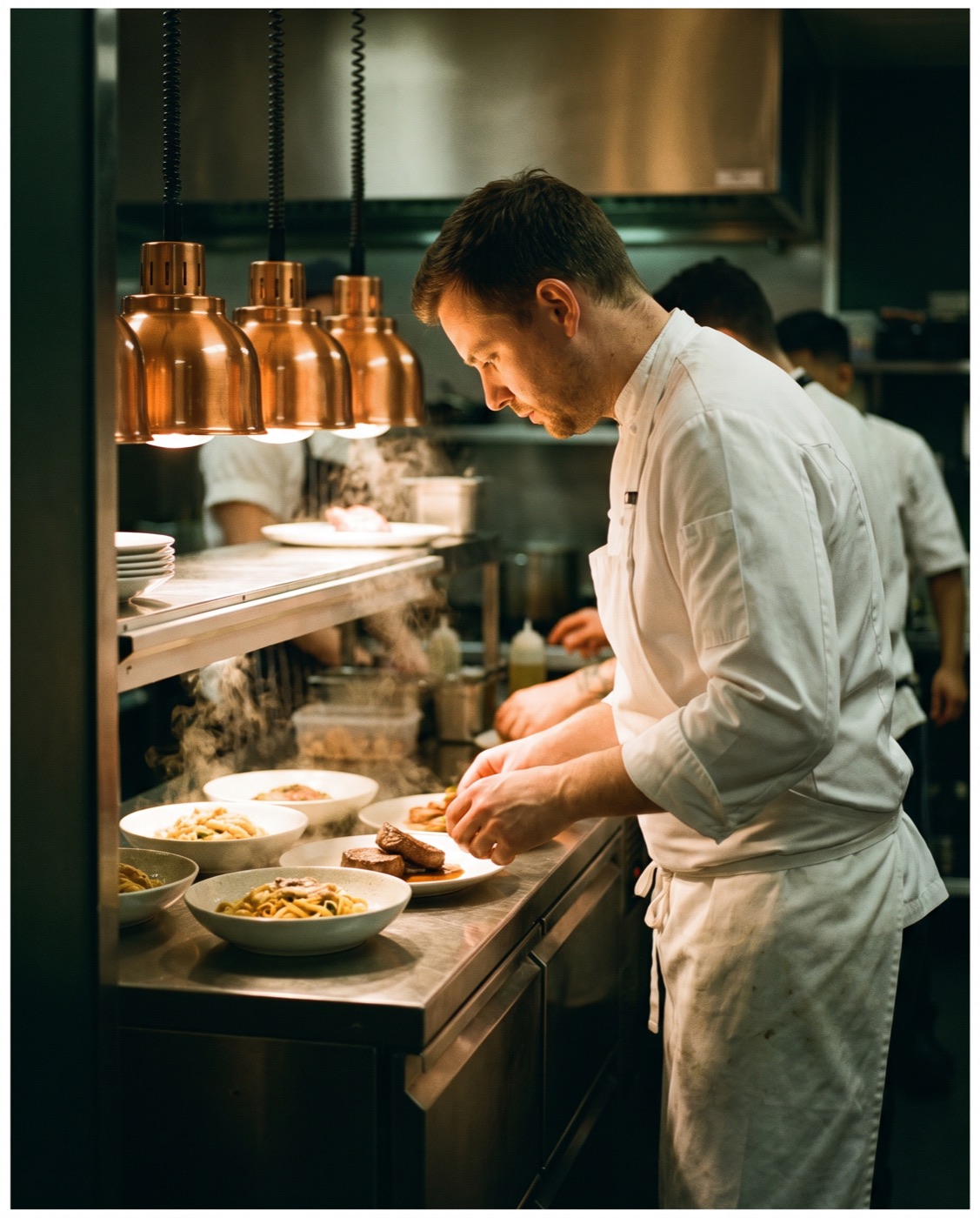 A chef in whites working the pass of a finished commercial kitchen during service